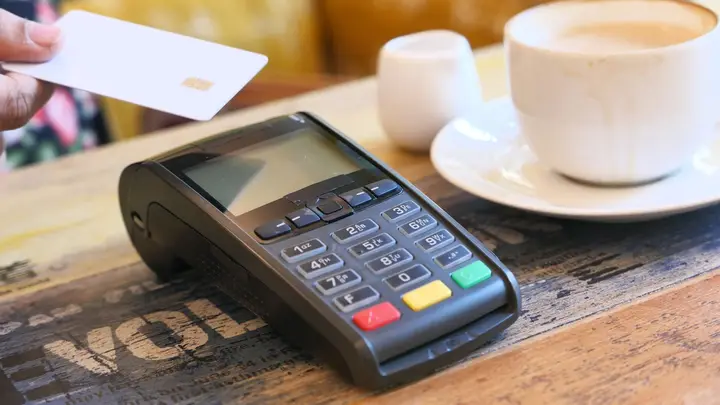 Maquininha de cartão na mesa ao lado de um café